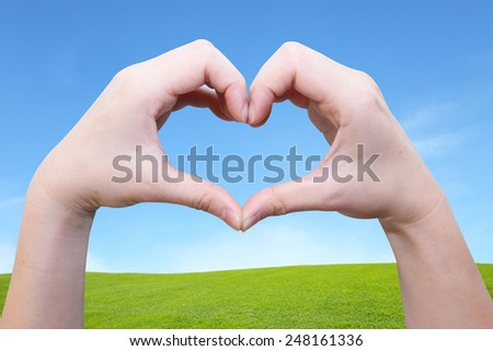 female hand in heart shape on the green field