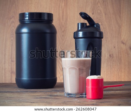 Whey protein powder in scoop  and plastic shaker on wooden background. Selective focus, shallow DOF