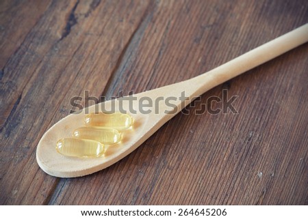 Cod liver oil omega 3 gel capsules in wooden spoon. Selective focus, shallow DOF