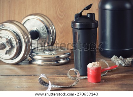 Whey protein powder in scoop with  plastic shaker on wooden background