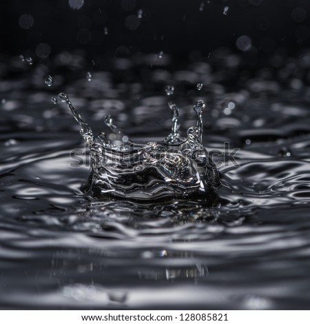 A water drop forms a crown as it splashes into a pool of water.