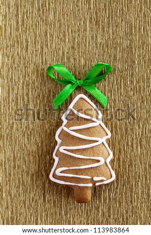 Christmas tree background. Ginger and Honey cookie fir tree with white sugar decoration and green bow on the gold wrapping paper background