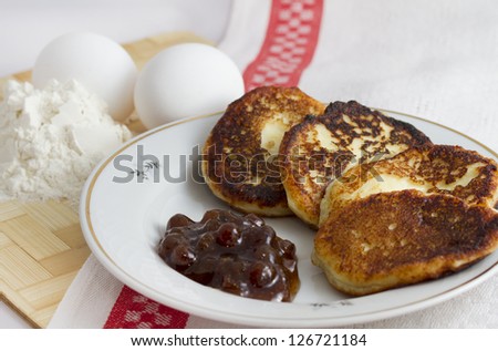 Curd pancake on a plate with strawberry jam and a handful of flour and egg