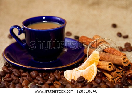 A cup of coffee with milk, coffee beans, mandarin slices and cinnamon sticks