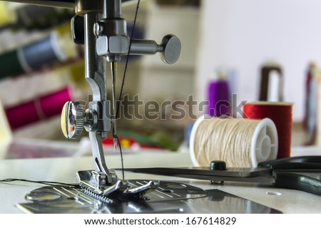 foot sewing machine with needle and thread in the background spools with colored threads
