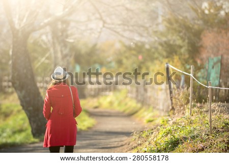 Woman wear red coat walking along the road with sunshine light.
