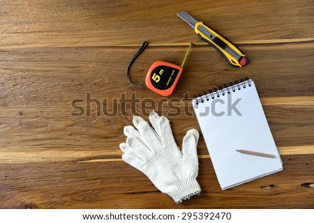 Blank note papers cutter cotton glove measure tape and pencil objects on a wooden desk in Top view.