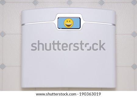 A white, digital bathroom scale displaying a happy face emoji.