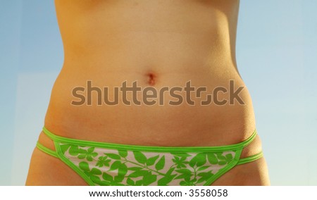 woman`s slim tanned belly isolated on blue sky