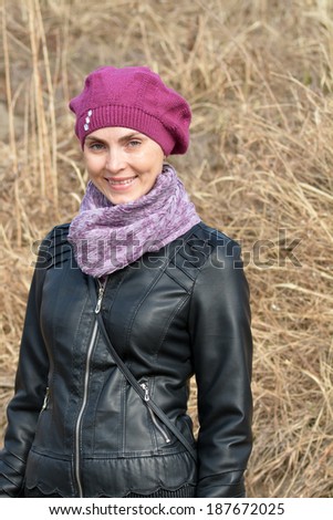 Woman in pink beret and black leather jacket against the background of dry grass