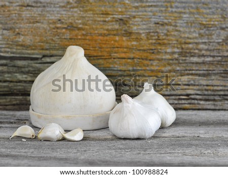 Garlic bulbs and cloves with a ceramic garlic keeper on a barn board background.