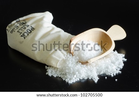 Rock salt spilling from a bag with wooden scoop