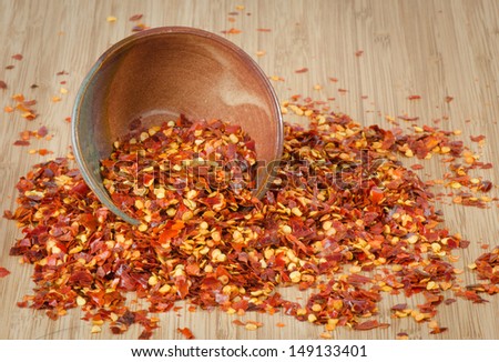 Crushed chili peppers spilling from a pottery bowl on a bamboo surface