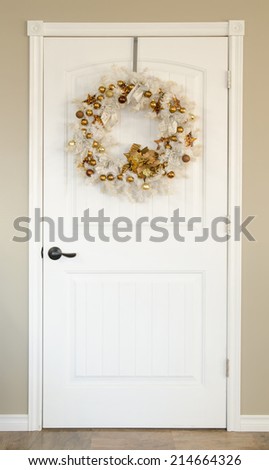 A white door with a white Christmas wreath with gold ornaments