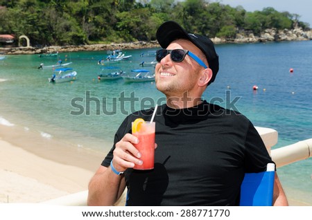 Young Caucasian man drinks cocktail at ocean beach resort during  summer vacations