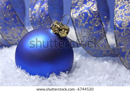 Blue christmas ball with a curly golden blue ribbon in snow
