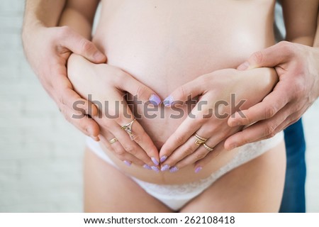 Male and female hands and big belly of pregnant woman. Woman and man making heart shape from hands. Couple in love awaiting for their first child. Mother and father. Family concept. Wife and husband.