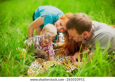Happy family having fun outdoors in spring garden. Father, mother and child kissing in grass. Family concept. Picnic. Woman, man holding little boy in hands. Laughing, smiling people playing with son