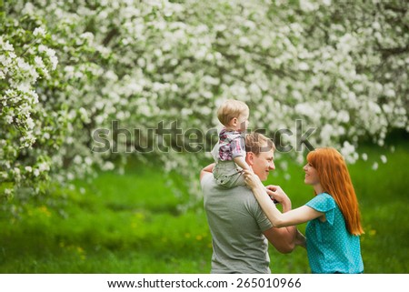 Happy family having fun outdoors in spring blooming garden. Father, mother and child. Family concept. Picnic. Woman, man holding little boy in hands. Laughing, smiling people playing with son