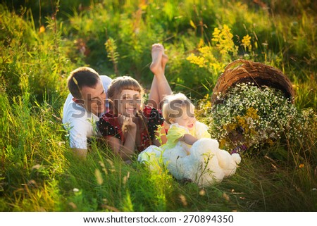 Happy family having fun outdoors in spring field. Father, mother and child kissing in grass. Family concept. Picnic. Woman, man, little girl. Laughing, smiling family playing wiith daughter. People