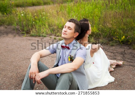 wedding couple sitting on ground. love symbols on pavement. hearts. people in love. happy bride and groom portraits. man and woman sitting back to back outside on road. newlyweds. wedding day