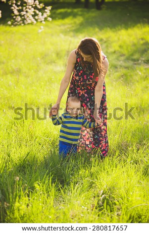 baby walking in green park holding hands of mother. happy little child playing outside with parents. first steps of infant. beautiful boy in spring blooming garden having fun with mom.