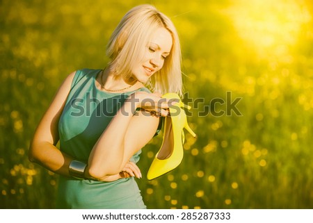 Beautiful young woman standing outside holding yellow trendy shoes in hands. Pretty blonde girl  with her shoes in summer park. Woman and fashion. Portrait of young lady in sunlights outdoors. Sunset.