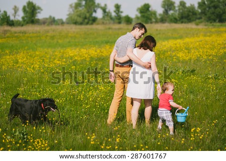 Happy family walking with black labrador dog in summer field. Father, mother, son holding hands. Family lifestyle. Togetherness. Child playing with parents and dog outside. Summer or spring day.