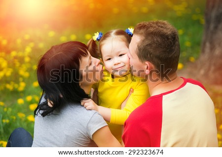 Mum and dad kissing cheeks of daughter. Happy family concept. Portrait of beautiful kid playing outside with parents.Young family spending time outdoor on a summer day.