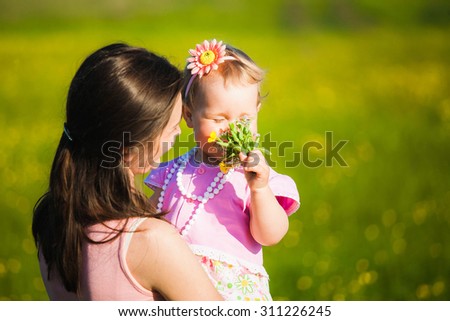 Little girl smelling field flowers. Family enjoying nature on spring or summer warm day outside.