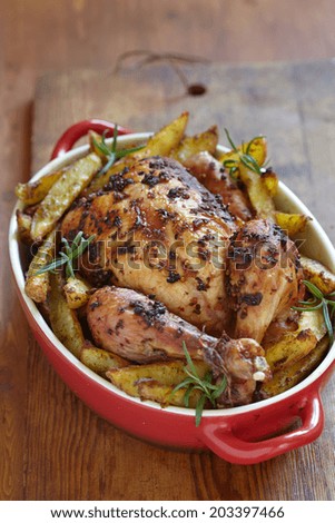 Whole roasted chicken with potatoes in red baked dish