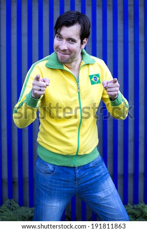 man in yellow sports jacket in front of blue wall is pointing his fingers toward camera and smiles