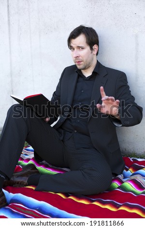 businessman reading a book outdoors and points with his finger that he doesnt want to be interrupted