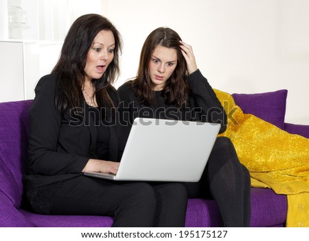 two woman sitting on purple couch and looking surprised at a laptop