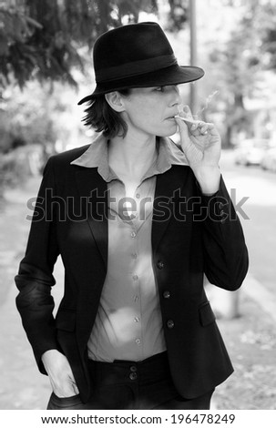woman in suit and hat is smoking a cigarette