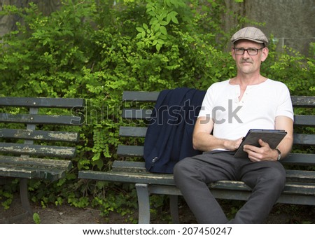 man sitting on a bench in a park with tablet in his hand