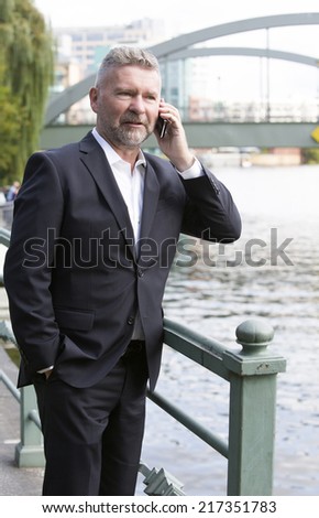 businessman in a suit standing in front of a bridge and speaking on the phone