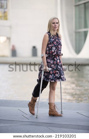 blonde woman in a dress walking with crutches