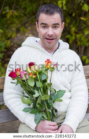 handsome man sitting outside on a bench with a bouquet of roses