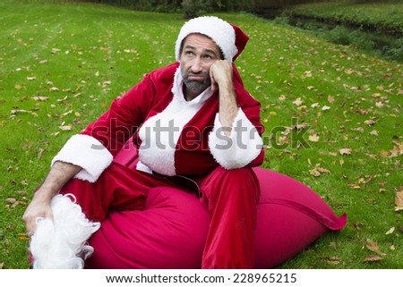 Santa Claus sitting in a park on a sack and looking exhausted