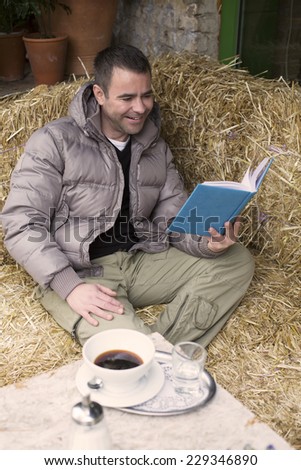 handsome man sitting outside in a cafe and reading a book