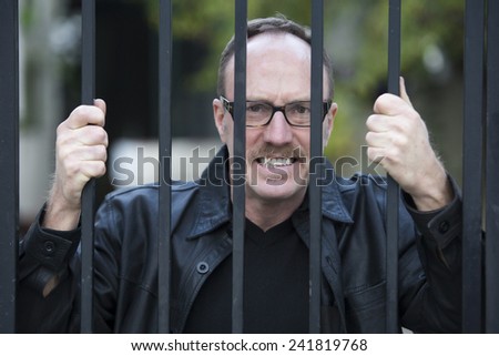 man standing behind iron bars and looking upset
