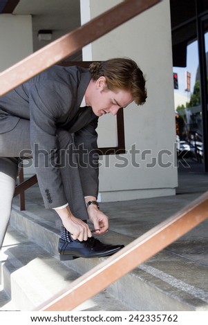 businessman outside at stairs ties his shoelaces
