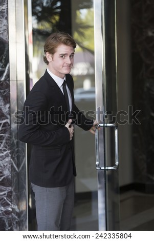 man in suit opens a door and smiles