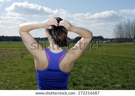 backside of young woman on a green field fixing her ponytail