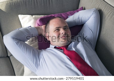 fat man in shirt and tie lying on couch and smiles