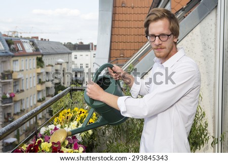 red-haired handsome young man watering flowers on balcony