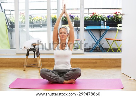 blond woman doing yoga in her living room with her eyes closed