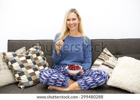blond woman sitting on couch and eating cherries