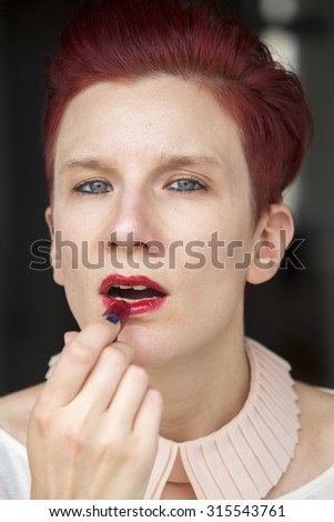 portrait of red-haired woman putting red lipstick on
